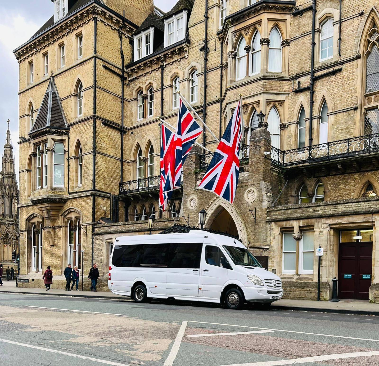 A white minibus parked in front of a building adorned with British flags.
